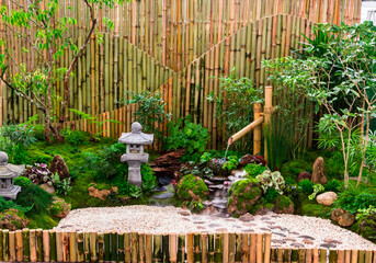 Minimal Japanese garden in home with small stone lantern and bamboo fountain and moss and flowers.
