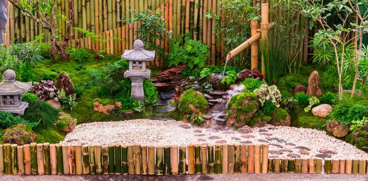 Minimal Japanese garden in home with small stone lantern and bamboo fountain and moss and flowers.
