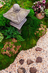 Minimal Japanese garden in home with small stone lantern and bamboo fountain and moss and flowers.
