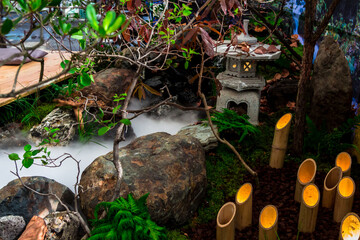 Minimal Japanese garden in home with small stone lantern and bamboo fountain and moss and flowers.
