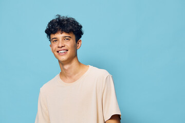 Young man smiling against a light blue background wearing a casual beige t shirt, exuding confidence and happiness in a cheerful atmosphere Ideal for lifestyle themes