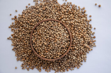 Coriander seeds in a wooden plate on a white background