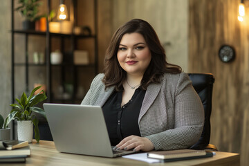Plus size woman with a large bust is sitting at a desk with a laptop. 