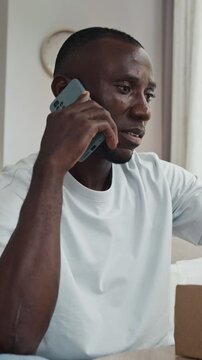 Vertical shot of male black client talking to support service of online store via smartphone while getting wrong parcel
