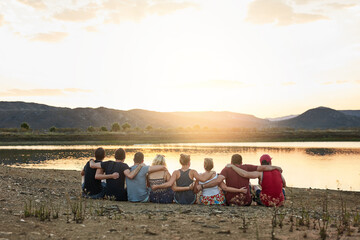 Back, hug and view with friends at lake together for outdoor holiday, travel or vacation in nature. Break, relax or trip and group of people embracing with horizon on water for calm, peace or quiet