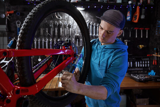 Closeup of hipster man bike mechanic removing rear wheel at garage workshop
