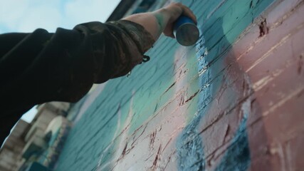 Close-up, below view of hand of unrecognizable male street artist detailing pink and red tag on brick wall with blue spray paint - Powered by Adobe