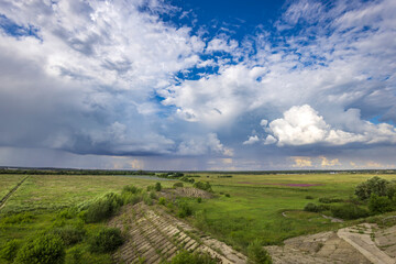 A sweeping view of lush greenery meets dramatic clouds, illuminated by the waning sunlight, showcasing nature's beauty in a serene, open landscape.