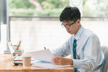 A man wearing glasses and a blue shirt is sitting at a desk with a piece of paper in front of him. He is looking at the paper and he is focused on it