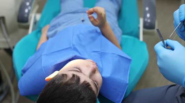 kid in dental office. dentist checking child teeth using tools mouth mirror and scalar.crying with tears, sad boy is afraid.doctor looking at screen,tooth filling treatment.kid in chair being examined