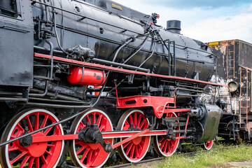 Rusty old steam train showcasing intricate details at a historic railway site on a cloudy afternoon