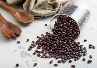 Dry raw organic purple beans in glass jar with wooden utensils and kitchen towel on light...