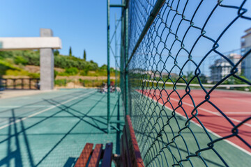Fototapeta premium A chainlink fence with an iron lock of an outdoor tennis court next to a wooden bench