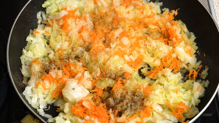 Finely chopped cabbage and carrots are stewing in a pan. Ideal for culinary and healthy eating content.