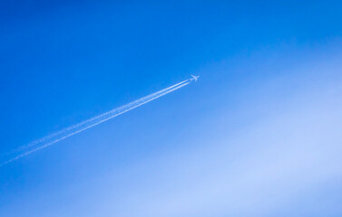 Far shot of a white jet leaving a contrail against a blue sky with white clouds