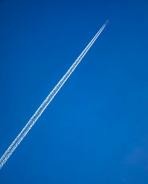 Dramatic contrail with texture from a jet in a diagonal moving from ower left to upper right against brilliant solid blue sky
