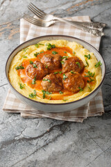 Meatballs with spicy sauce with a side dish of corn porridge close-up in a bowl on the table. Vertical