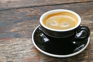 Cup of frothy hot black coffee isolated on wooden table