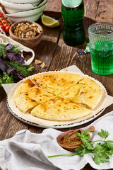 Traditional Ossetian Cheese Pie on Rustic Wooden Table with Fresh Herbs and Nuts