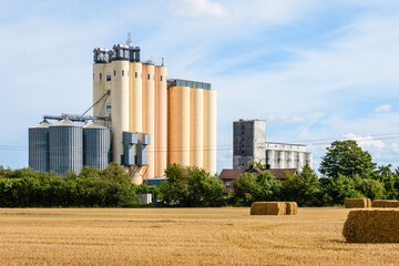 Two grain tower silos in the countryside, a smaller and older gray one next to a more recent and...