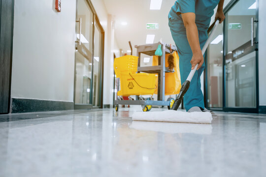 A Safety sign with caution phrase. Happy young housekeeper mopping the floor with a mop and cleaning products to clean dust in a hospital corridor.