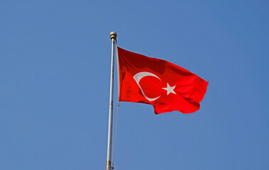 Turkish national flag on blue sky background. The flag on a flagpole flutters in the wind. The white star and crescent moon on red background.