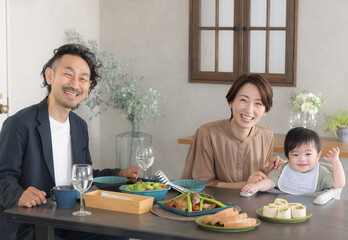 レストランや自宅で食事する赤ちゃんと夫婦　カメラ目線　ニコニコ笑顔の赤ちゃん