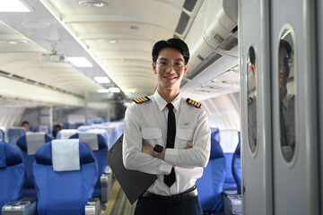 Portrait of smiling pilot standing with his arms crossed in the aisle of an airplane