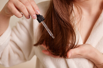 A young woman applies a drop of oil from a pipette to her hair, close-up. Vitamins, keratin for treatment, strengthening and growth of hair. Problems with dandruff, hair loss. Hair care concept