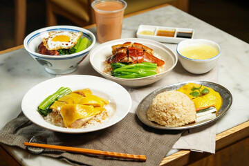 Boneless Hainanese Chicken Rice, Roasted Duck, Poached Chicken, BBQ Pork with Fried Egg, baby kailan, milk kopi and chopsticks isolated on napkin table side view of assorted asian foods
