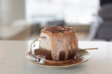 Iced coffee with frothy cream overflowing chocorate topping with powder.