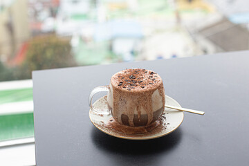 Iced coffee with frothy cream overflowing chocorate topping with powder.