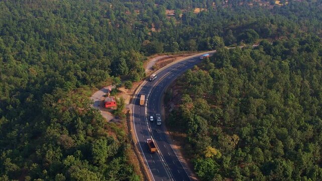 aerial view of the winding road with several vehicles, including trucks and buses, traveling along it. he road surrounded by the dense forest. In Jharkhand India