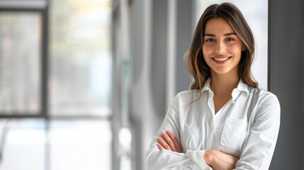 Confident businesswoman with crossed arms smiling in modern office, facing camera, embodying success in professional attire with sleek hairstyle.