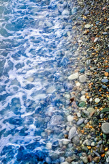 Blue waves roll onto the multicolored sea pebbles Black Sea coast. Beautiful natural background. Top view, vertical photo.
