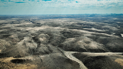 Aerial view of the vast arid landscape of Iona National Park in Angola showcasing its rugged hills and winding riverbeds under a cloudy sky