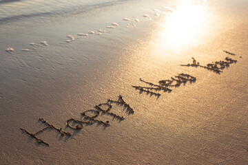 Happy new year written on sandy beach