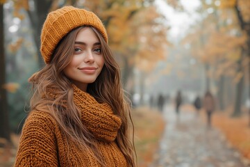 Young woman in an orange knit hat and sweater smiles amidst autumn trees on a misty day, copy space for text, fashion model, autumnal clothes, wardrobe changing