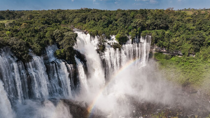 Fototapeta premium Kalandula Waterfall cascades in Angola with vibrant rainbow above lush greenery during daylight