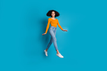 Full size photo of pretty young girl running jump wear trendy yellow outfit isolated on blue color background