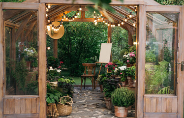 Cozy wooden greenhouse with string lights, filled with plants and flowers, featuring an easel and...