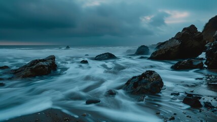 Obraz premium The ocean's waves cascade over dark rocks as clouds gather, creating a serene yet dramatic atmosphere at dusk