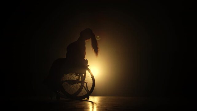Woman performing graceful para dance movements whirling on a wheelchair under the stage backlit. Determination and disability concepts.
