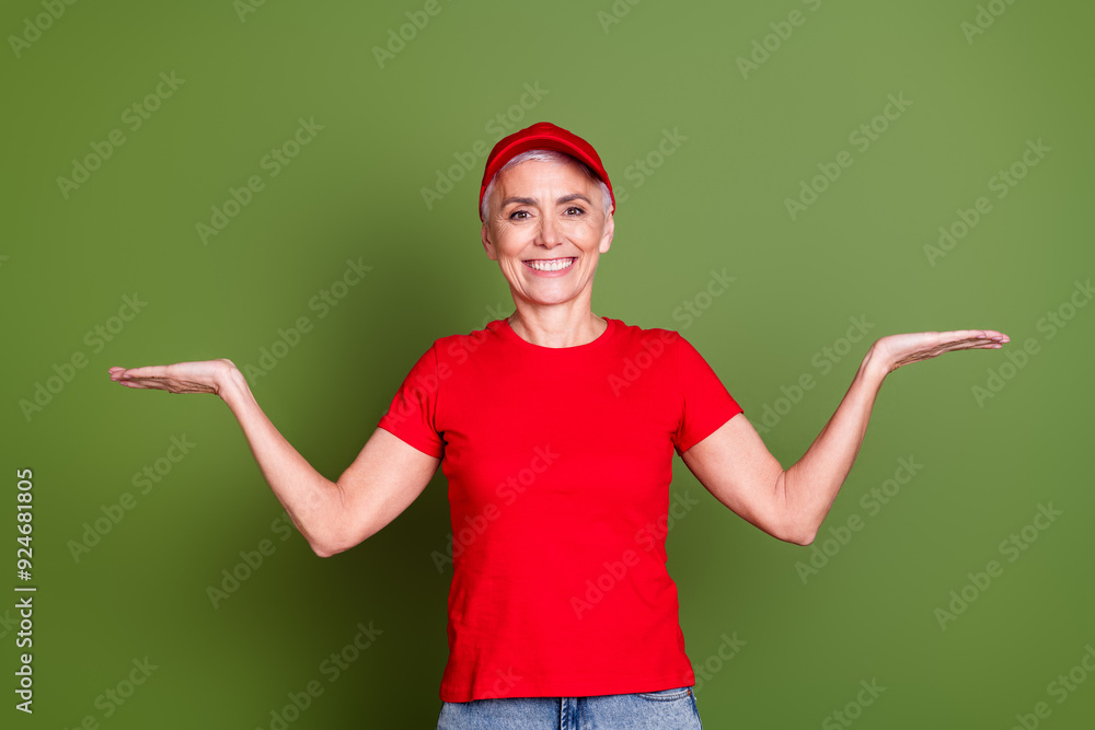 Sticker Photo of lovely pensioner lady delivery service employee compare empty space dressed red uniform workwear isolated on khaki background