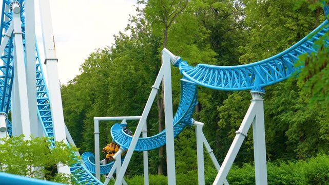 Loop roller coaster in an amusement park. Roller coaster cart with people riding it goes through passing spiral corkscrew receding into the distance