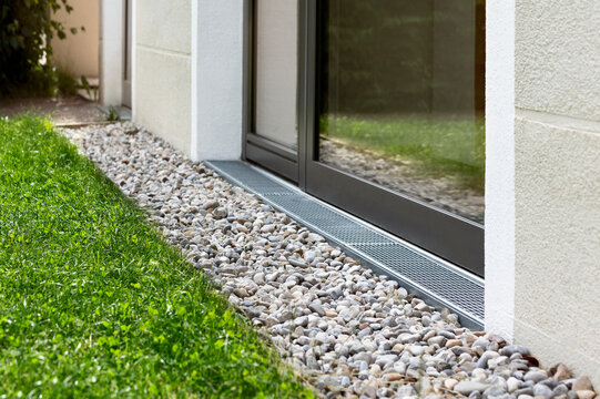 Drainage Stone Gravel Pebbles Floor Outside Building with Mesh Grate by Window to Absorb Water and Ventilate Wall of House. French Drain System. 
