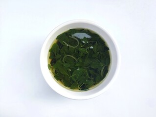 Moringa leaves soup in the bowl isolated on white background. Indonesian food, vegetarian cuisine 