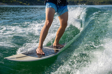 Close-up of male legs on wakesurf board. Turquoise water. Wakesurfing on lake.