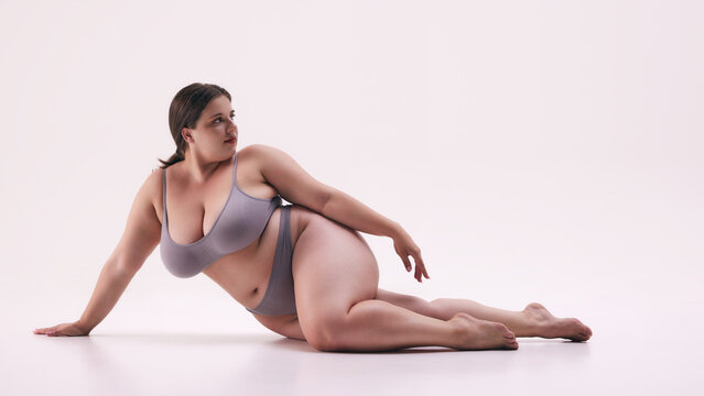 Strong woman, plus size model wearing underwear, posing lying on floor, show her body with pride against white studio background. Concept of natural beauty, body positivity, self love, treatments. Ad