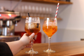 Two cocktails with ice served on a wooden bar counter in a modern cafe, a hand taken one of them